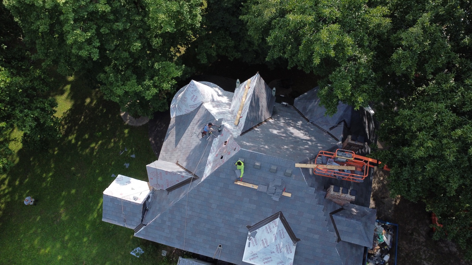 Aerial view of a roofing crew installing a new roof, underlayment down and shingles staged